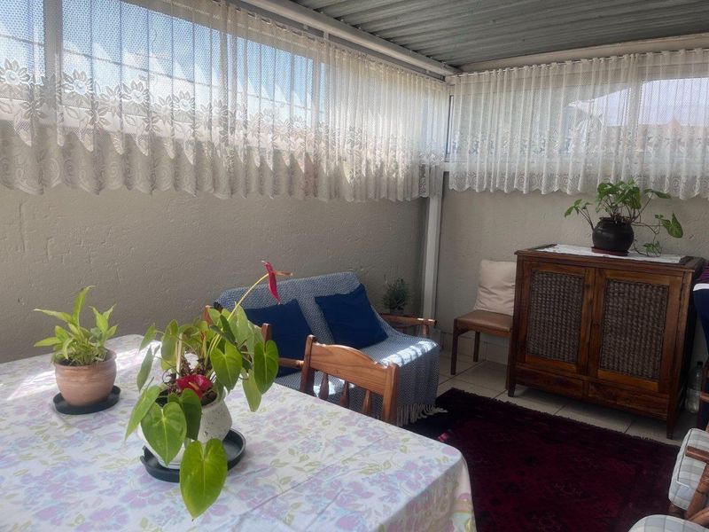 A covered patio area featuring tiled flooring and large windows, providing a functional outdoor living space.