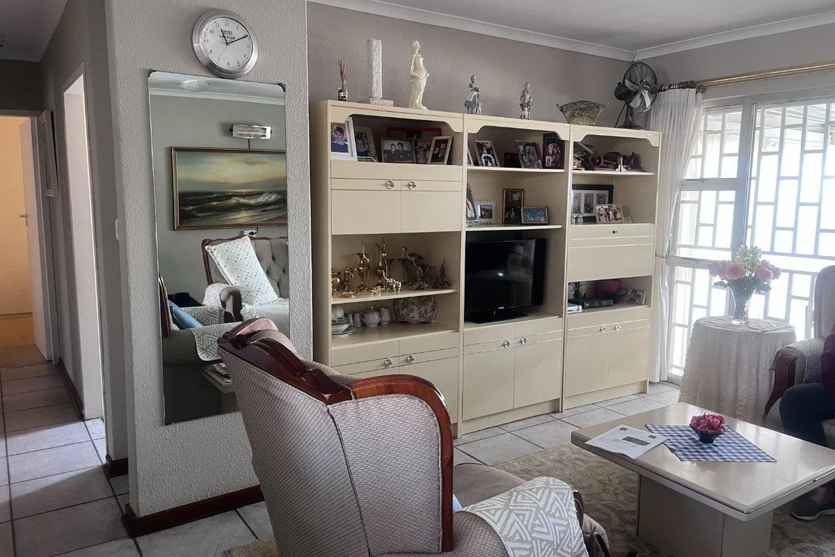 A living room featuring tiled flooring, a large built-in wall unit, and access to an outdoor area through a sliding door with security gate.