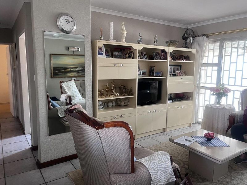 A living room featuring tiled flooring, a large built-in wall unit, and access to an outdoor area through a sliding door with security gate.