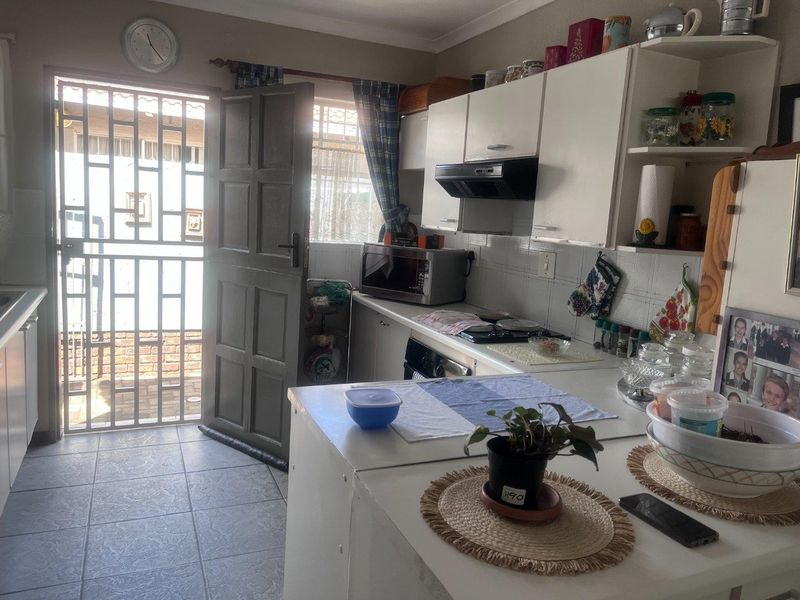 A functional kitchen featuring built-in cabinetry, a hob, and an extractor fan, with direct access to an exterior area through a security gate.