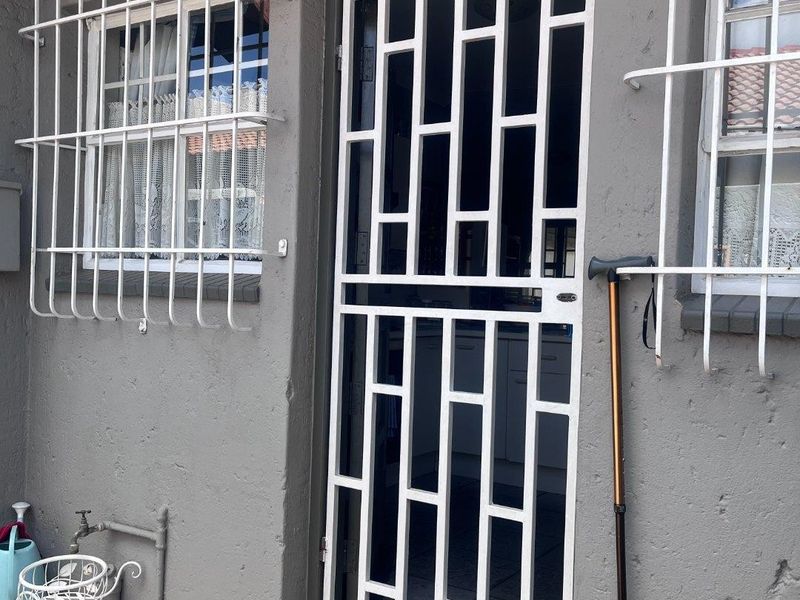 Rear exterior entrance featuring a white security gate, protective window bars, and an outdoor tap, showing signs of wear on the exterior wall finish.