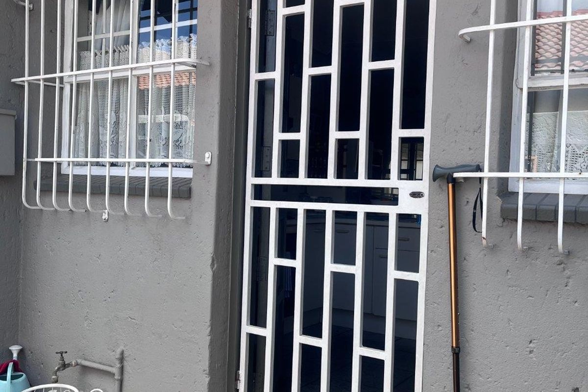 Rear exterior entrance featuring a white security gate, protective window bars, and an outdoor tap, showing signs of wear on the exterior wall finish.