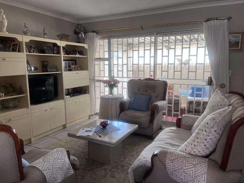 A comfortable living room featuring tiled flooring, cove cornicing, and a large sliding glass door with integrated security gate leading to the patio.