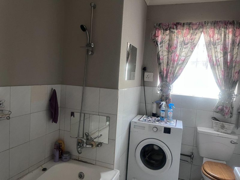 A functional bathroom featuring a bathtub with a handheld shower attachment, a toilet, and tiled walls, requiring some maintenance and cosmetic updates.