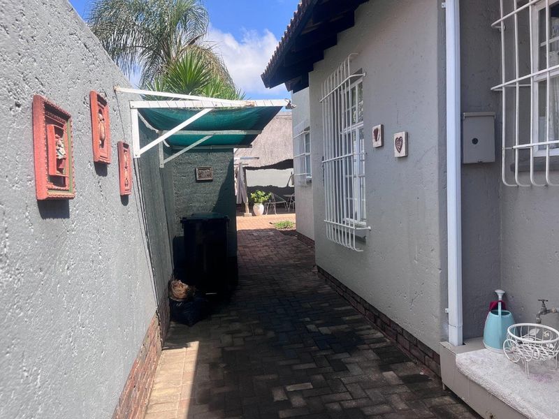 A paved side walkway leading to the rear garden area, featuring security bars on windows and a wall-mounted washing line.