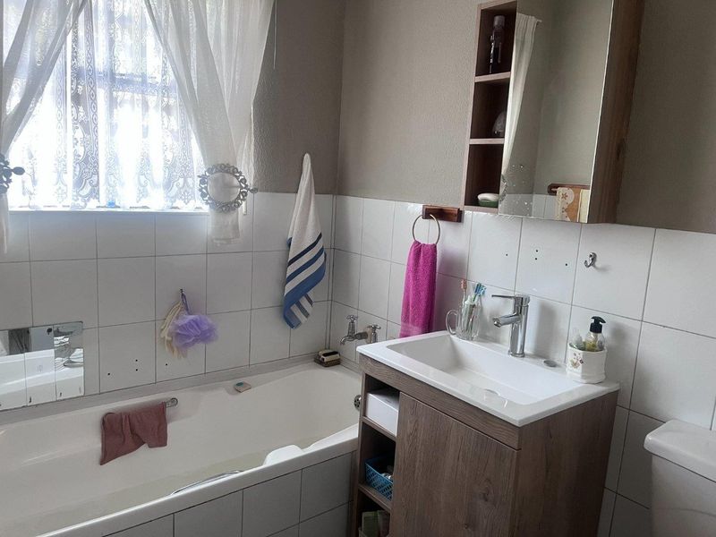 A functional bathroom featuring a built-in vanity with basin, a bathtub, and wall-mounted storage cabinet, finished with tiled splashbacks.
