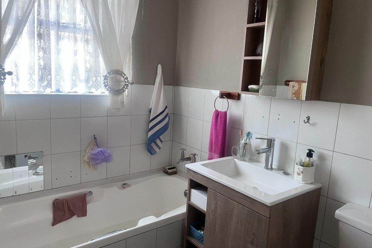 A functional bathroom featuring a built-in vanity with basin, a bathtub, and wall-mounted storage cabinet, finished with tiled splashbacks.