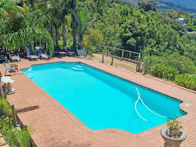 Outdoor swimming pool area featuring a brick-paved deck, timber fencing, and established garden surroundings with scenic views.