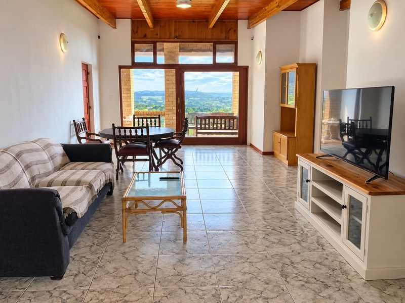 Spacious open-plan living and dining area featuring exposed timber ceiling beams, tiled flooring, and large sliding doors offering scenic landscape views.