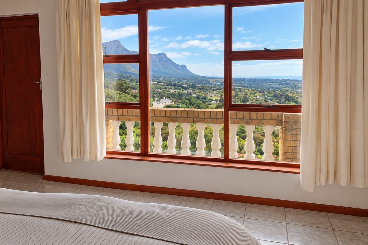 A bedroom featuring large timber-framed windows that offer expansive mountain and landscape views, complemented by a classic balustrade and tiled flooring.