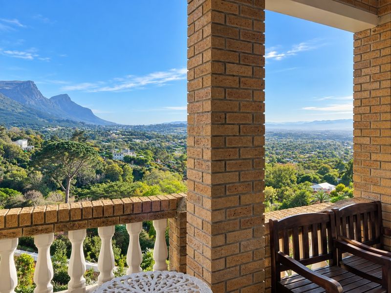 A covered balcony featuring brick pillars and a classic balustrade, offering expansive panoramic views of the surrounding valley and mountain landscape.