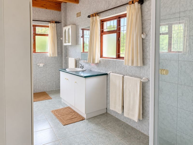 A functional bathroom featuring a vanity unit, tiled surfaces, and exposed timber ceiling beams, offering a dated aesthetic ready for modernization.