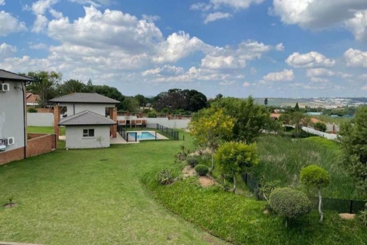 A spacious rear garden featuring a swimming pool, well-maintained lawn, and perimeter fencing, offering an open view of the surrounding landscape.
