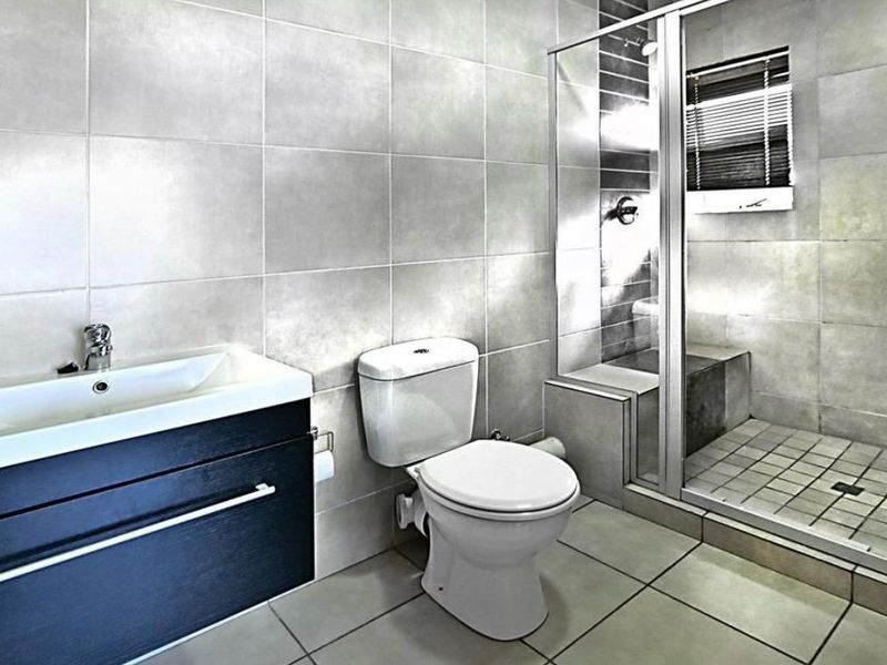 Modern bathroom featuring a vanity cabinet with basin, a standard toilet, and a glass-enclosed shower with tiled finishes throughout.