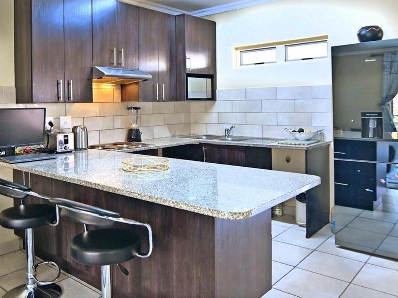 A functional kitchen featuring dark wood cabinetry, granite countertops, a stainless steel extractor fan, and a tiled backsplash with a breakfast bar area.