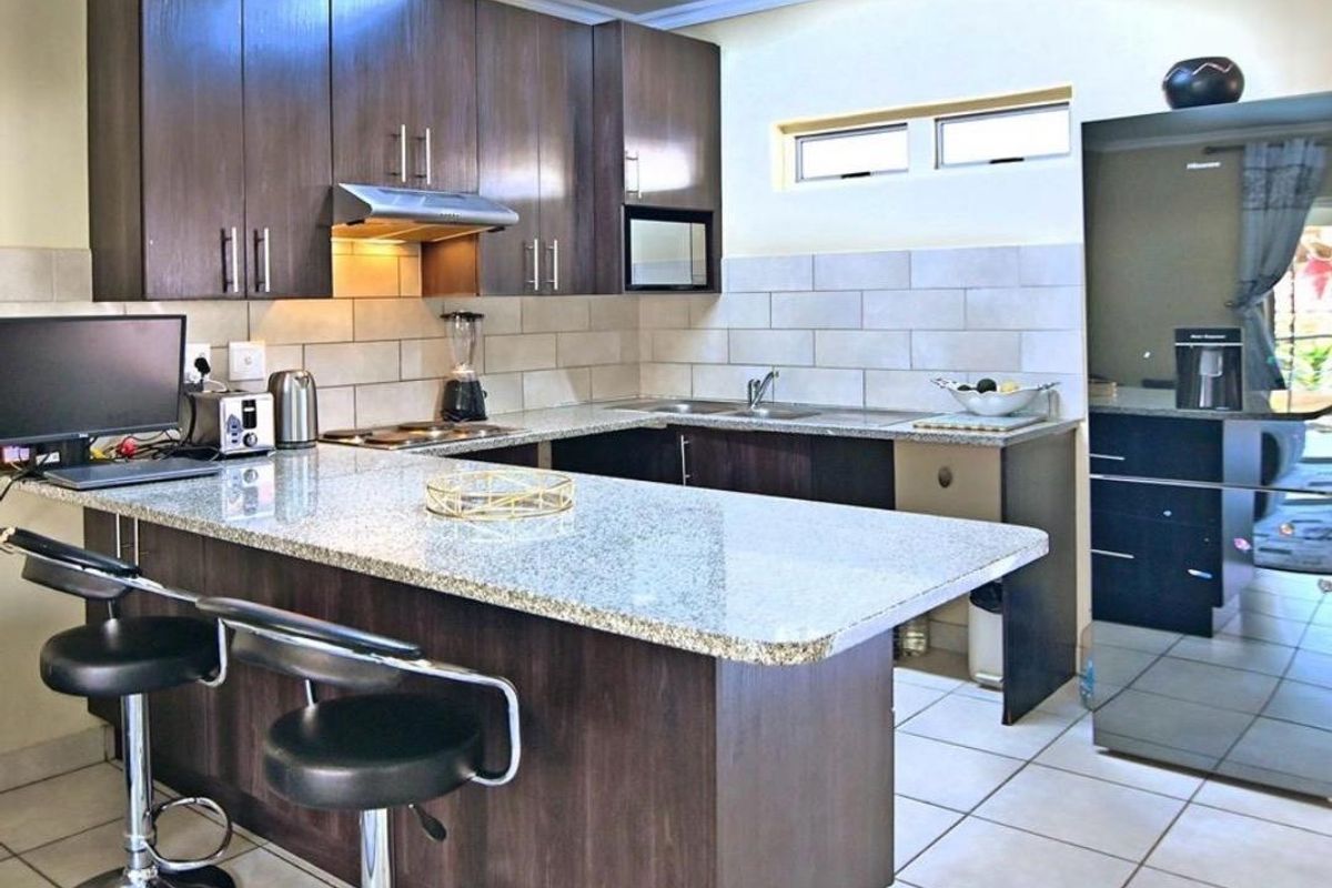 A functional kitchen featuring dark wood cabinetry, granite countertops, a stainless steel extractor fan, and a tiled backsplash with a breakfast bar area.