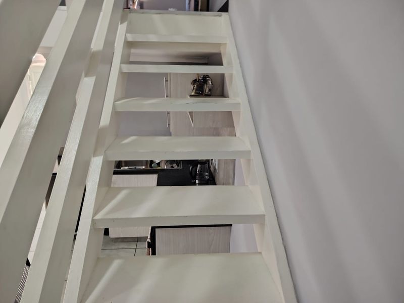 A view looking down a white painted staircase with a simple railing, providing access between levels in the apartment.