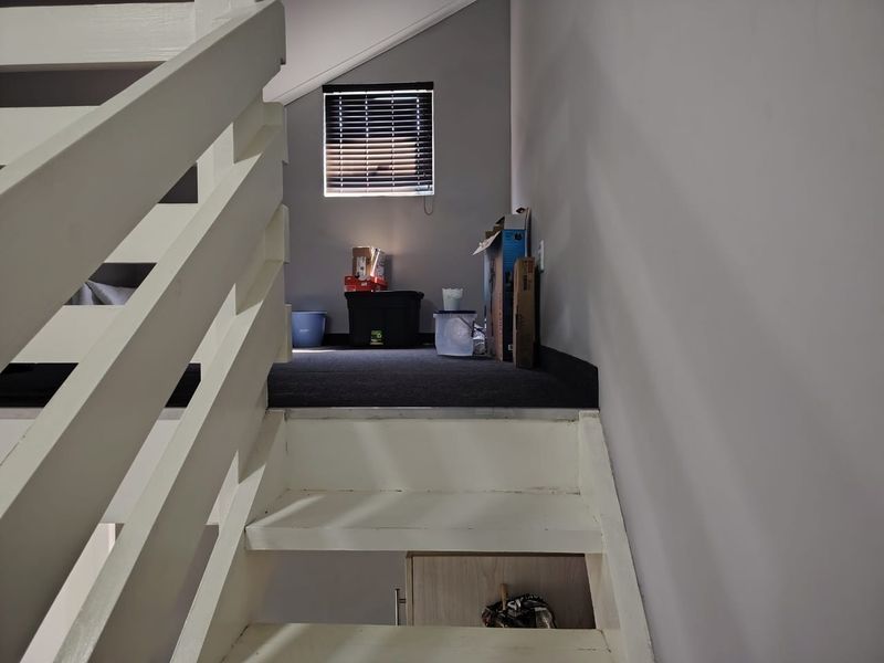 A view of an upper landing area featuring a staircase with white railings and a window with venetian blinds.