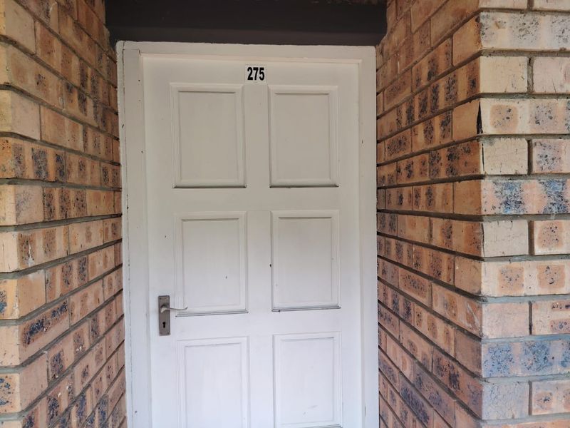 A residential apartment entrance featuring a white panelled door set within a face-brick exterior wall.