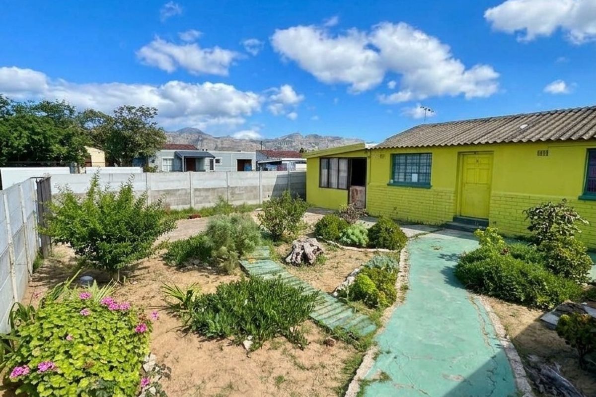 Rear exterior view of the property featuring a painted brick facade, tiled roof, and a landscaped garden with a concrete pathway.