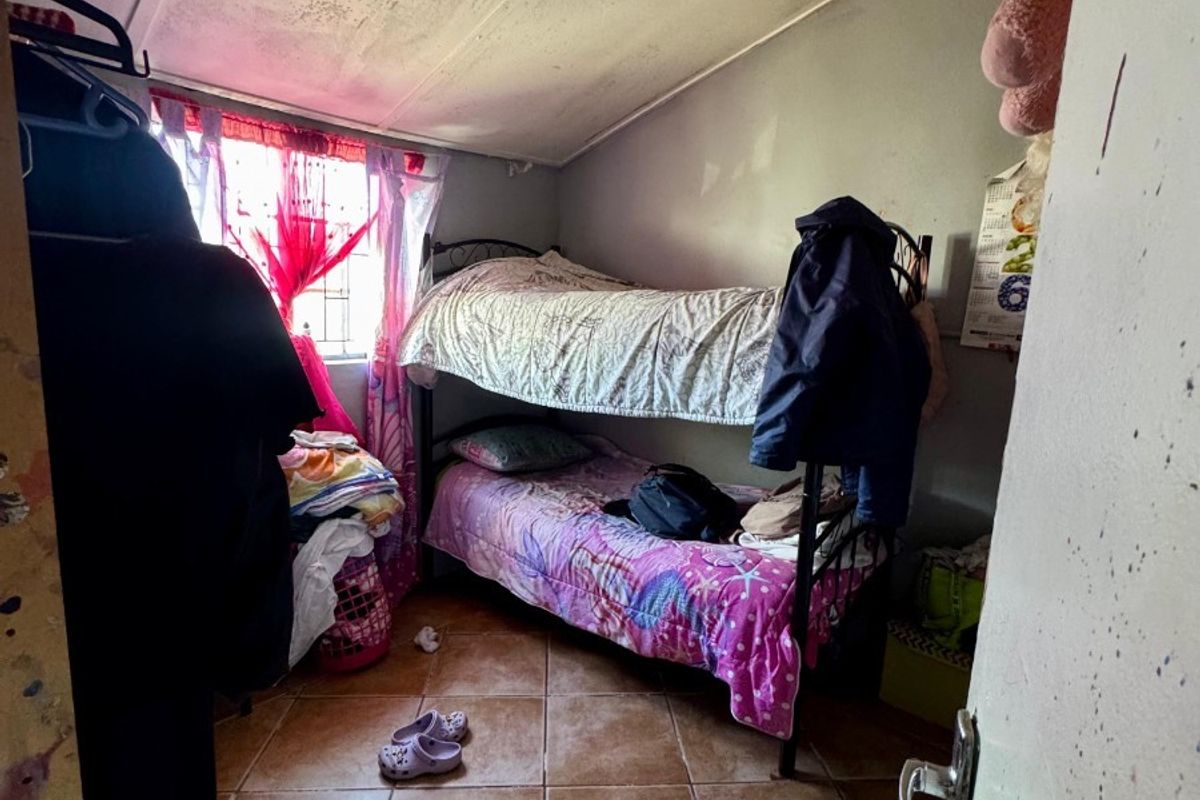 A compact bedroom featuring tiled flooring, a sloped ceiling, and security bars on the window, currently showing signs of wear and maintenance needs.