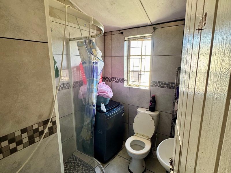 Compact bathroom featuring a shower enclosure, toilet, and pedestal basin with tiled finishes throughout.