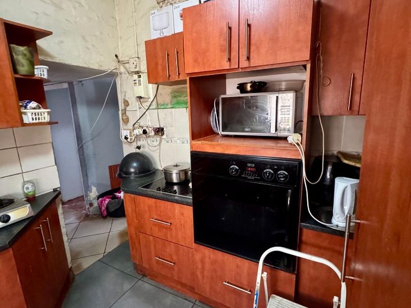 A dated kitchen featuring wood-finish cabinetry, built-in oven and hob, and tiled flooring, requiring cosmetic updates and repairs to wall finishes.