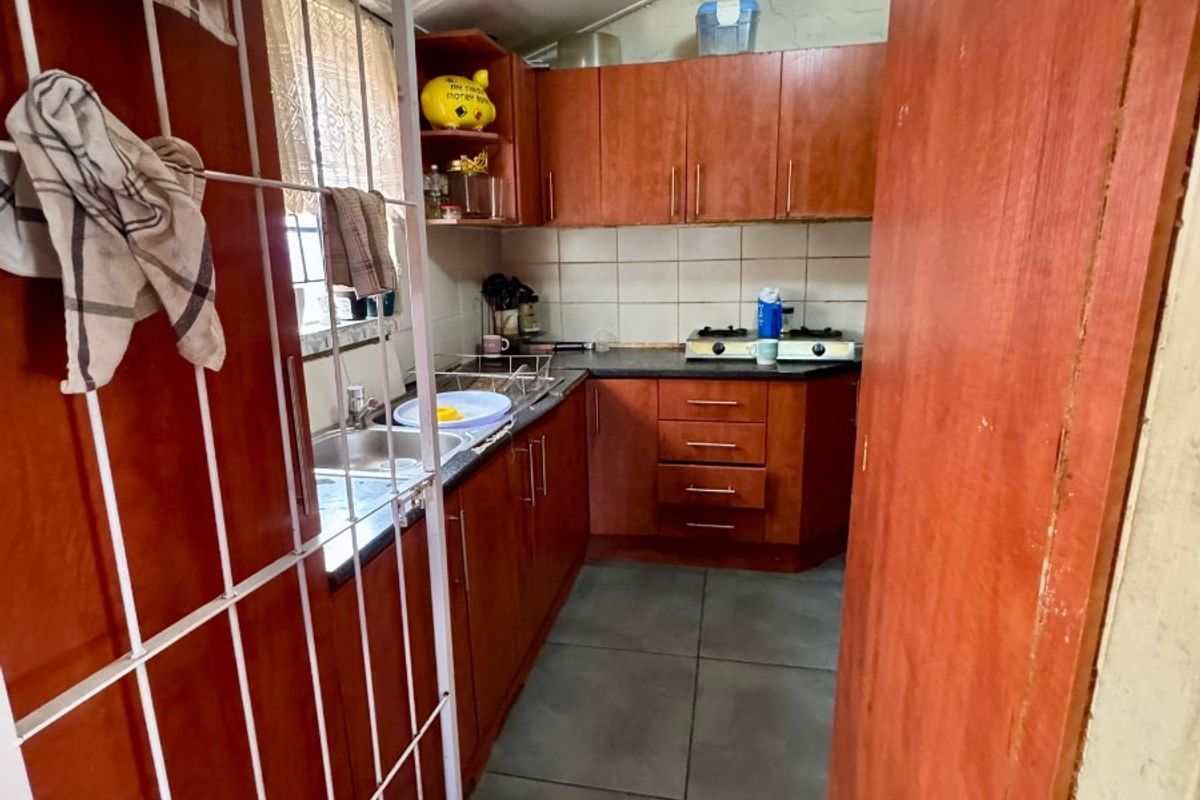 Compact kitchen featuring laminate cabinetry, built-in stove, double sink, and tiled flooring. The space would benefit from modern updates to finishes and lighting.
