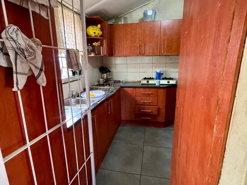 Compact kitchen featuring laminate cabinetry, built-in stove, double sink, and tiled flooring. The space would benefit from modern updates to finishes and lighting.