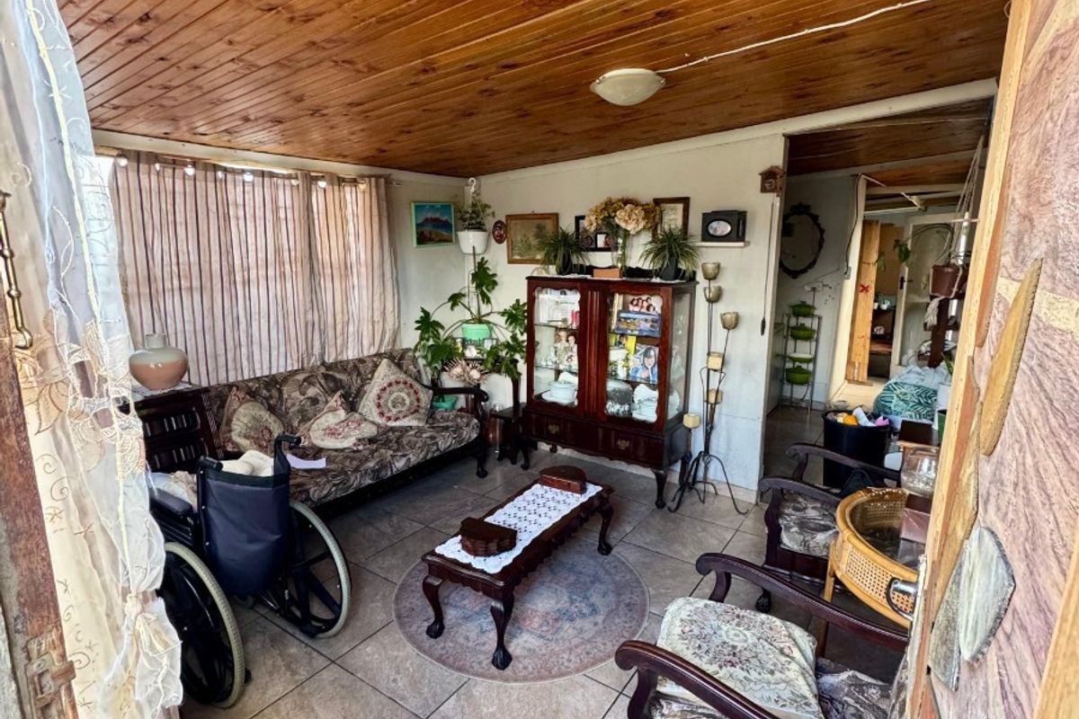 A living area featuring a timber tongue and groove ceiling and ceramic tiled flooring, providing a dated but functional space.