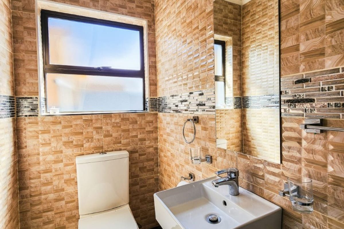 A modern, compact bathroom featuring full-height textured wall tiling, a wall-mounted basin with chrome fixtures, and a sleek toilet.