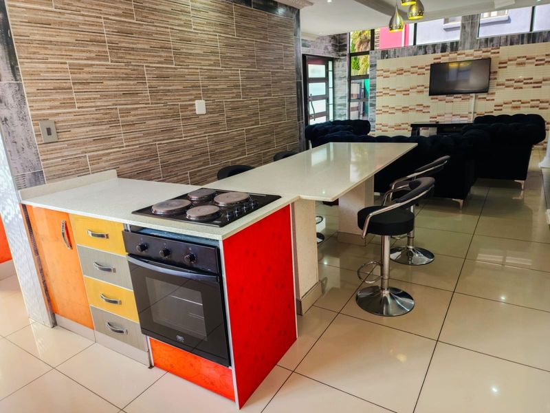 Open-plan living area featuring a kitchen island with built-in oven and hob, stone countertops, and modern tiled flooring throughout the space.