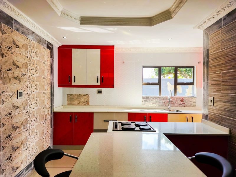 Modern kitchen featuring high-gloss red and white cabinetry, stone countertops, integrated hob, and decorative ceiling cornicing with recessed lighting.