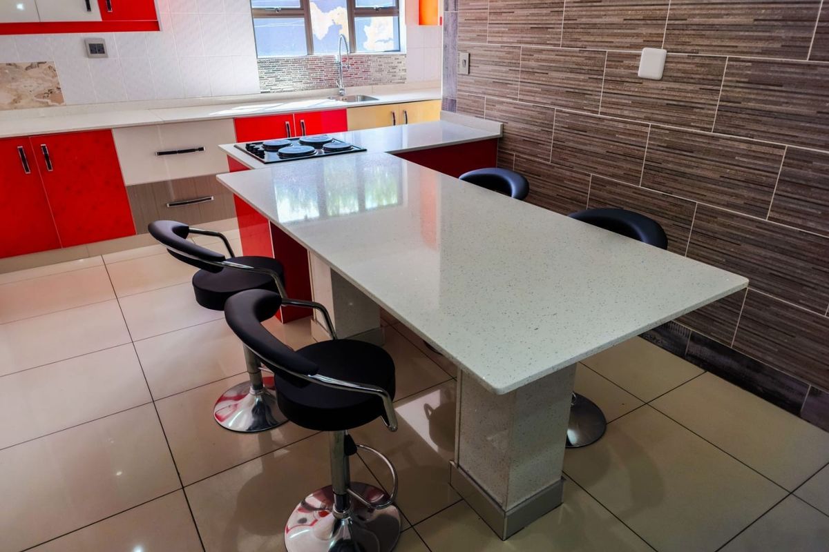 Modern kitchen featuring a central quartz breakfast bar, built-in hob, high-gloss cabinetry, and contemporary tiled feature wall with neutral floor tiles.