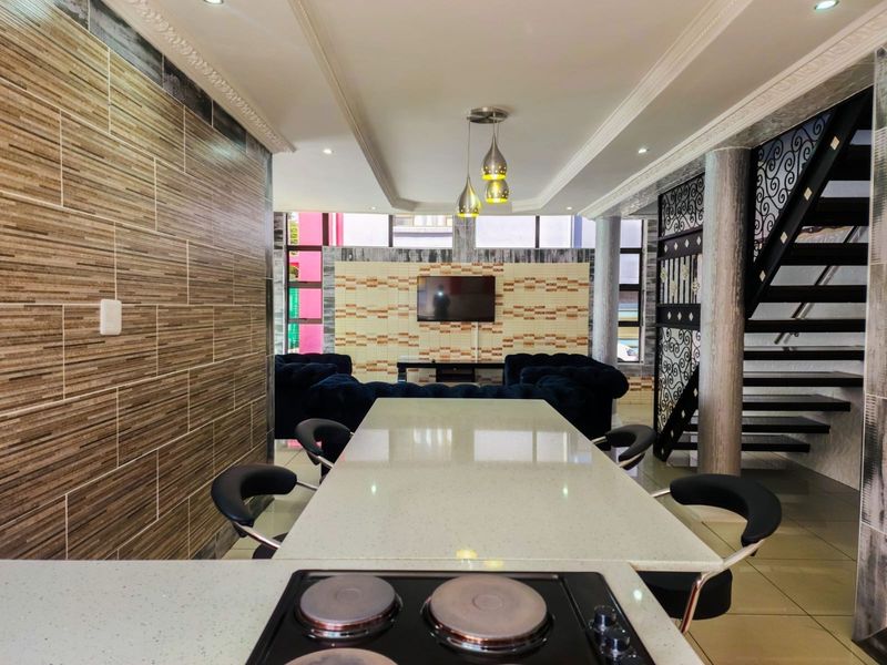 Open-plan living and dining area featuring a modern kitchen island with a built-in hob, decorative wall tiling, and a stylish staircase.