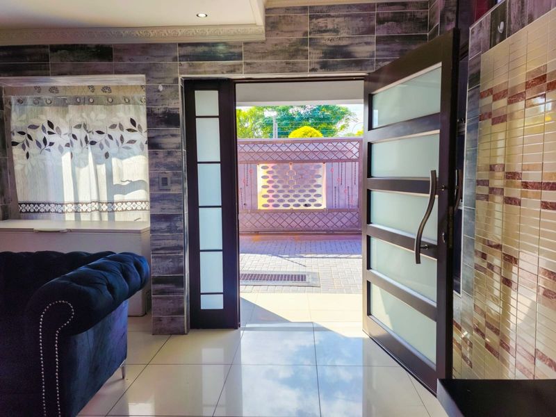 Entrance area featuring modern tiled flooring, decorative wall tiles, and a contemporary frosted glass panel door leading to the exterior.