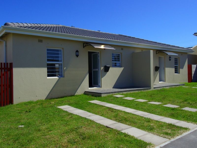 Front view of a modern single-story residential unit featuring a tiled roof, concrete driveway strips, and a small front garden area.