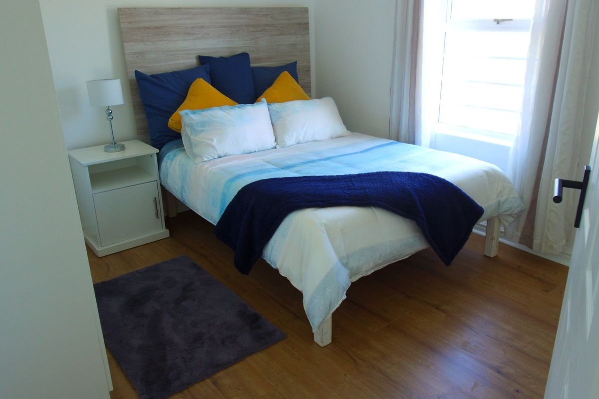 A well-lit bedroom featuring durable laminate flooring and a large window, providing a comfortable and functional living space.