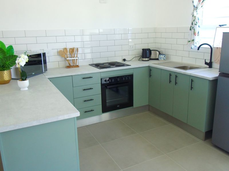 Modern kitchen featuring sage green cabinetry, subway tile backsplash, built-in oven, electric hob, and neutral tiled flooring.