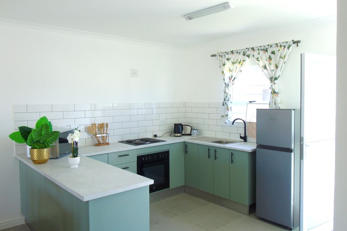 A modern kitchen featuring sage green cabinetry, white subway tile backsplash, built-in oven, electric hob, and a functional breakfast bar area.