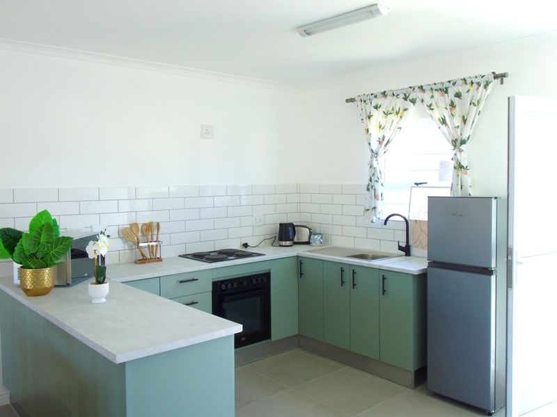 A modern kitchen featuring sage green cabinetry, white subway tile backsplash, built-in oven, electric hob, and a functional breakfast bar area.