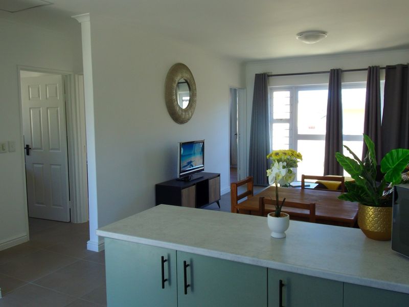 Open-plan living and dining area featuring tiled flooring, a functional kitchen island with laminate countertops, and access to natural light through sliding doors.