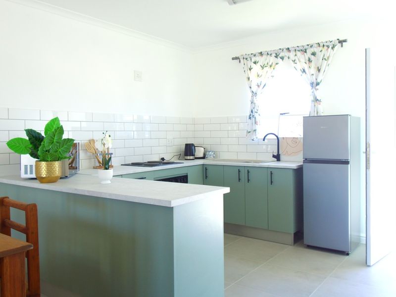 A bright, modern kitchen featuring sage green cabinetry, white subway tile backsplash, laminate countertops, and a functional layout with a breakfast bar.