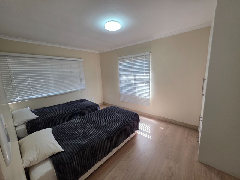 A bright bedroom featuring light-toned laminate flooring, built-in wardrobe storage, and venetian blinds on the windows.