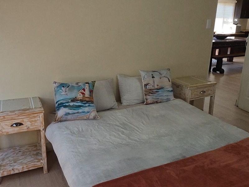 A bedroom featuring light-toned laminate flooring and neutral wall finishes, with a view leading into an adjacent living area.