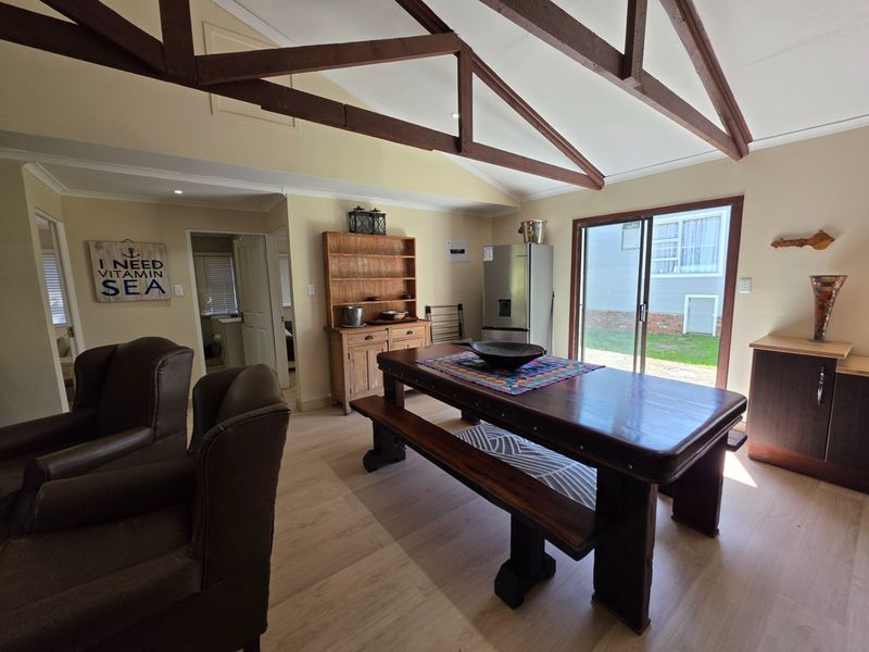 Open-plan living and dining area featuring exposed timber roof trusses, laminate flooring, and direct access to the rear garden via sliding glass doors.