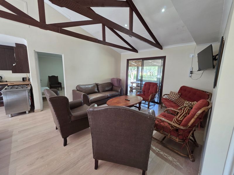 Open plan living area featuring exposed timber roof trusses, laminate flooring, and direct access to the patio through sliding glass doors.