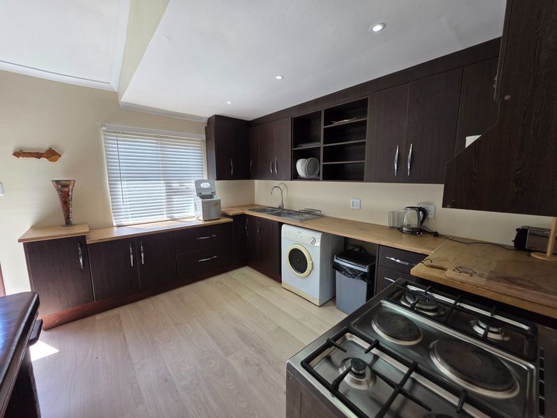 A functional kitchen featuring dark wood cabinetry, light laminate countertops, integrated gas hob, and light-toned laminate flooring with ample storage space.