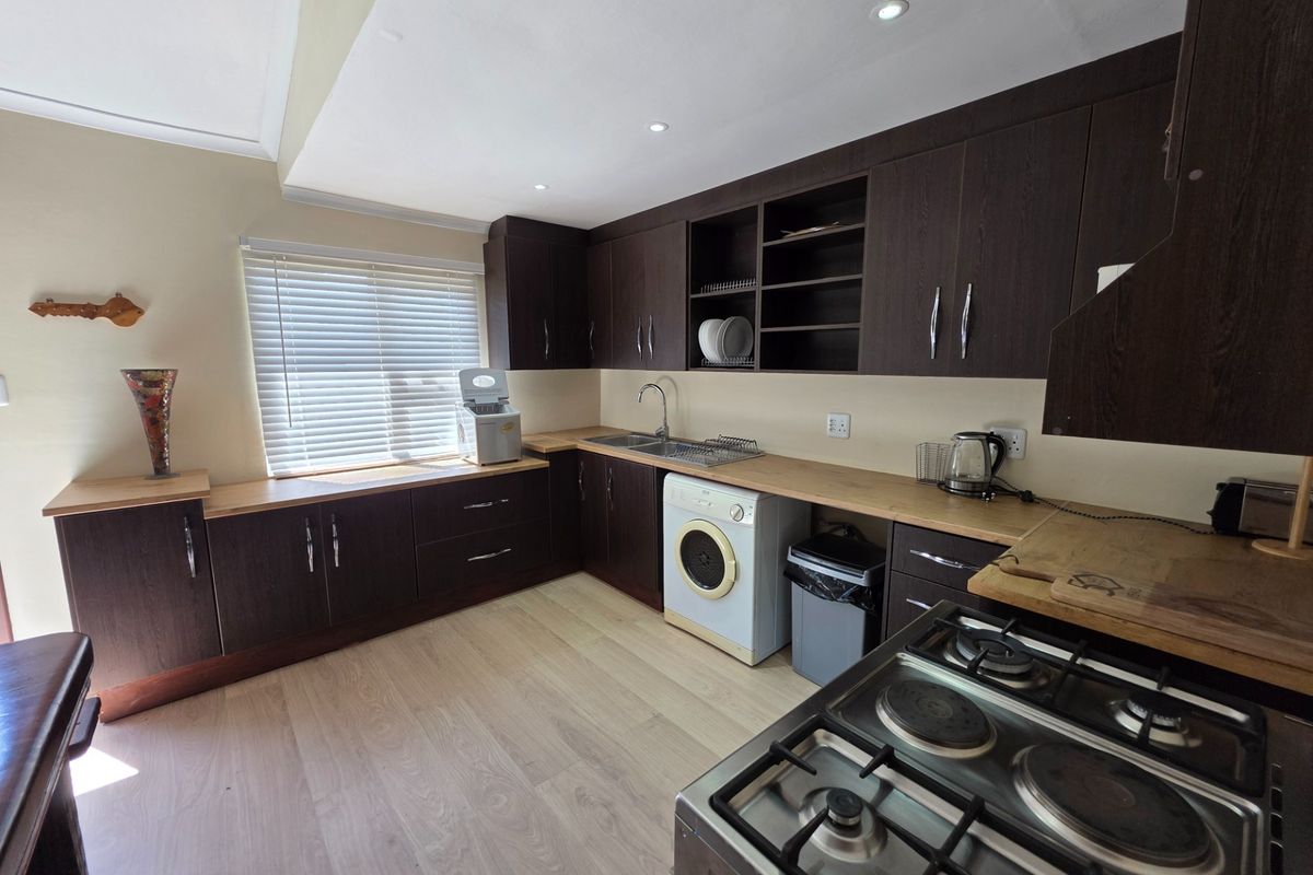 A functional kitchen featuring dark wood cabinetry, light laminate countertops, integrated gas hob, and light-toned laminate flooring with ample storage space.