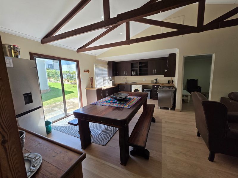 Open-plan kitchen and dining area featuring exposed timber roof trusses, laminate flooring, and direct access to the garden through a sliding glass door.